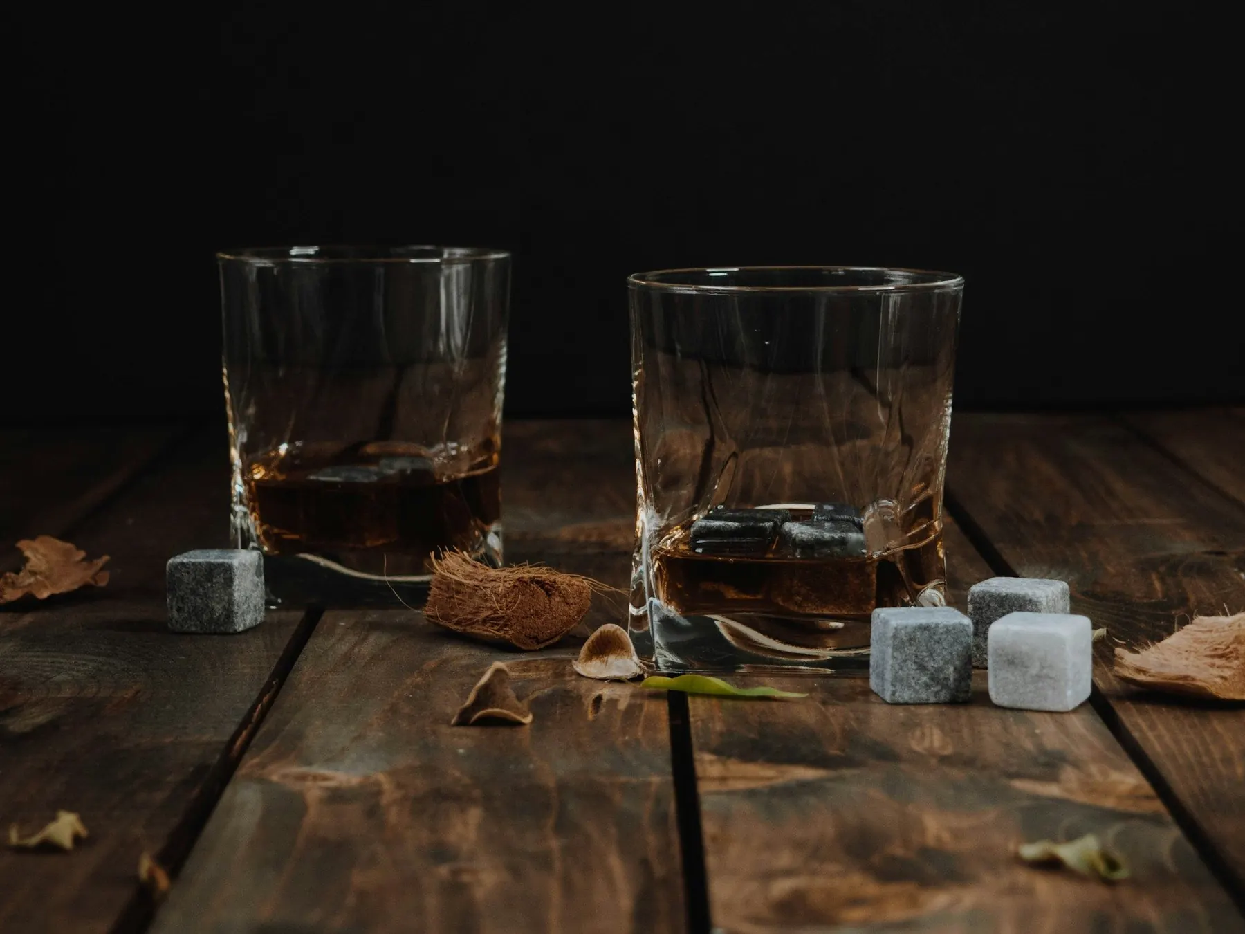 Zwei Whiskygläser mit Steinwürfeln auf dunklem Holztisch