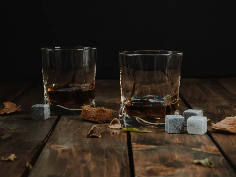 Zwei Whiskygläser mit Steinwürfeln auf dunklem Holztisch